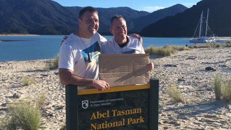 Two campaigners hold a sign saying 'Our beach' as they stand on a beach in New Zealand - 10 July 2016