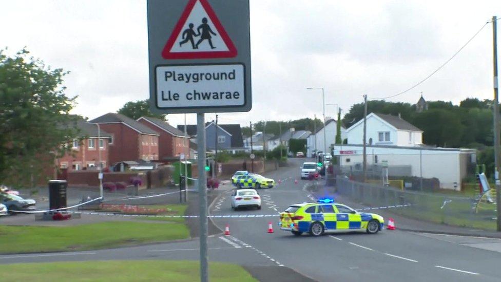 Police car and police tape across a road near a playground sign