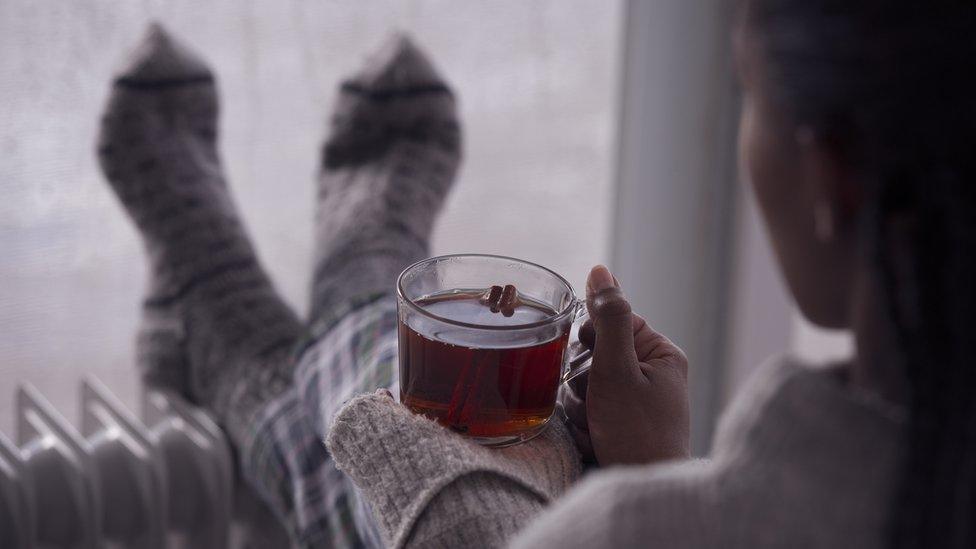 A person with a cup of tea with feet on radiator