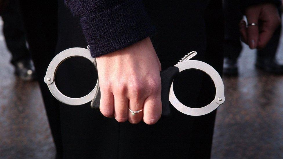 A close-up of a police officer holding a pair of handcuffs