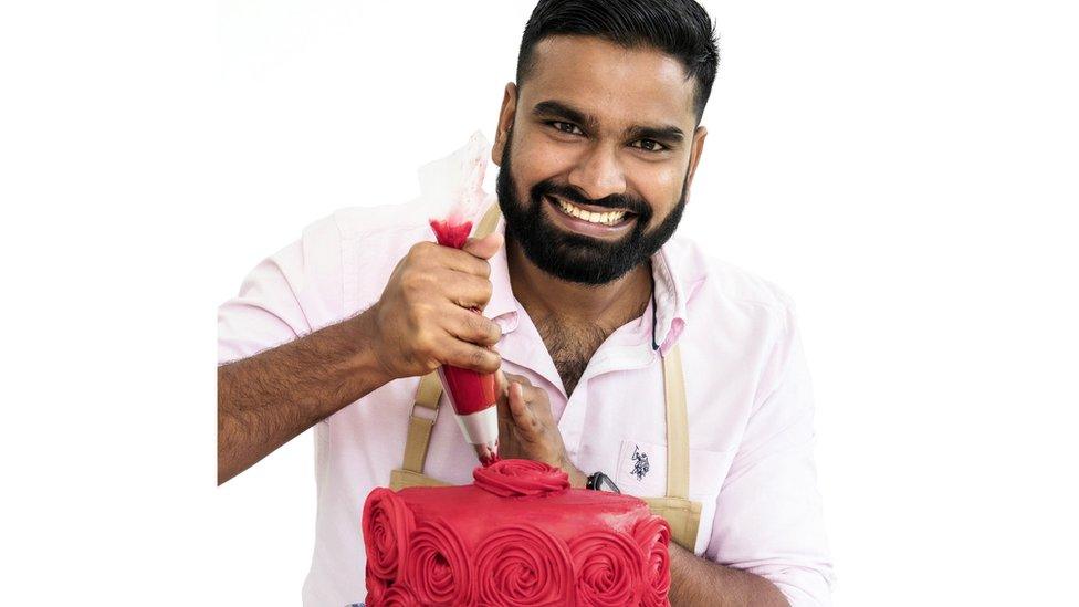 Antony smiles while icing a red cake with roses