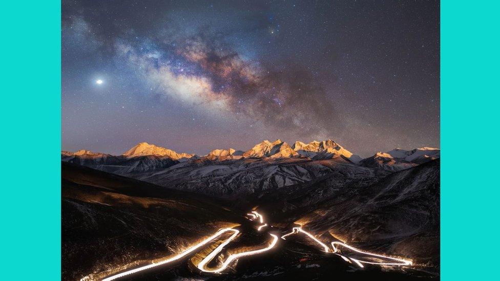 The illuminated National Highway 219, the highest national highway in the world, snakes through the foreground, mirroring the image of the Milky Way above