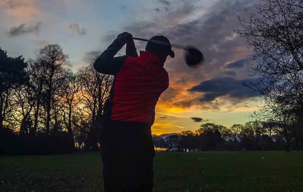 A golfer hits a ball on a golf course as the sun rises