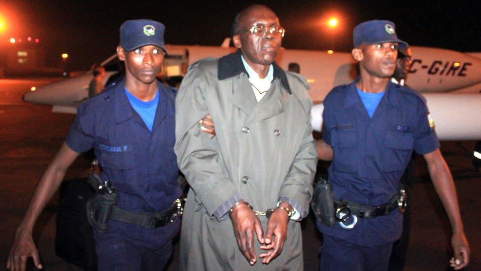 Leon Mugesera (C) is escorted handcuffed by policemen to a police vehicle on the tarmac as he arrives at Kigali International Airport late on January 24, 2012