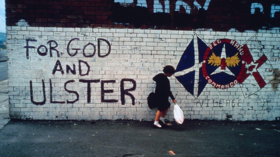 A woman stood in front of a loyalist mural, which reads "for God and Ulster"