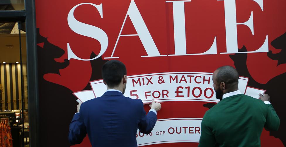 Men fix a "sale" sign to a shop front