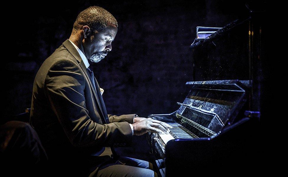 Adrian Lester as Gil playing the grieving son at his father's funeral