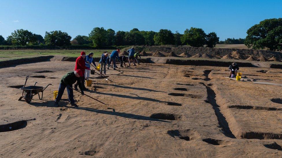 Fully excavated post holes on the east side of the hall, and volunteers cleaning the trench for post excavation photography