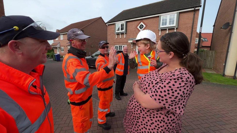 Harry, being held by his mum, high-fives a bin man