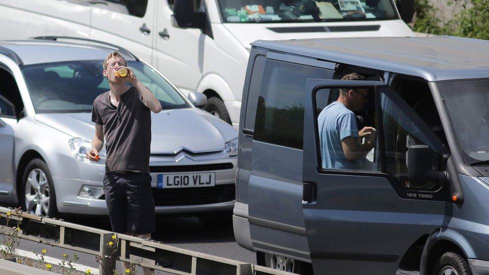 Drinking water while standing next to a car stuck in traffic