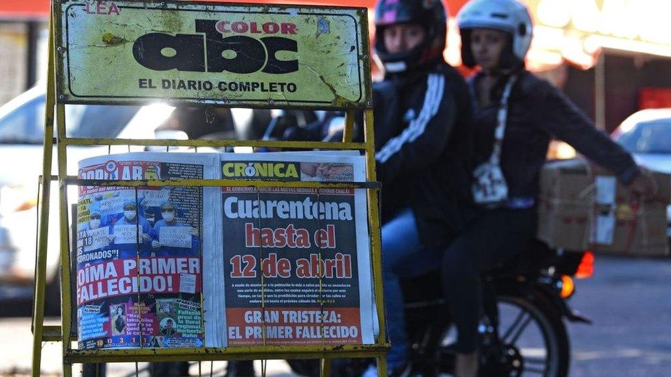 A motorcycle rides near a stall displaying front pages of newspapers with the news of the first person killed by the new coronavirus, in Asuncion on March 21, 2020.