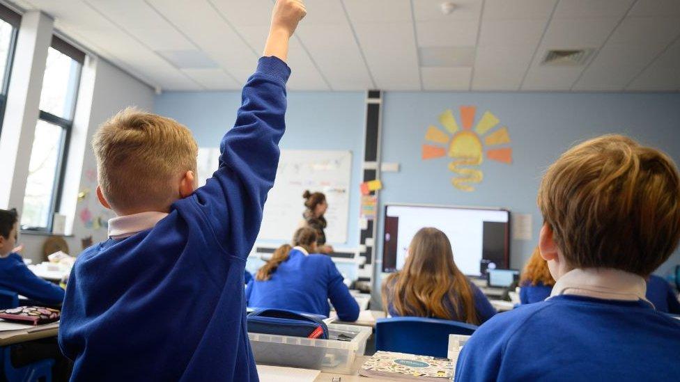 Schoolboy with his hand up in the air in a classroom