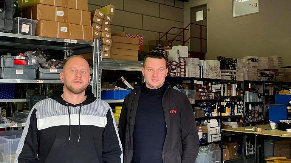 Two men with short dark hair stand in an industrial unit