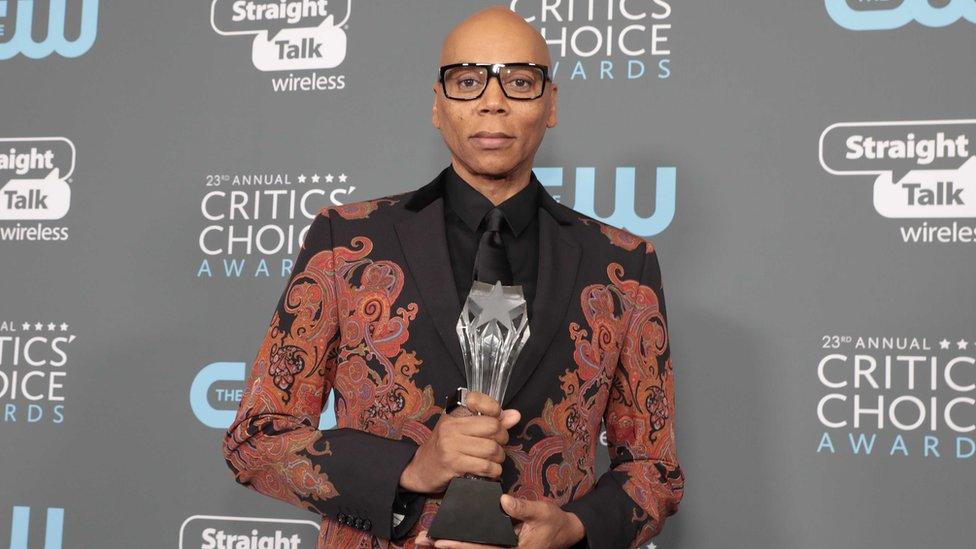 A close-up of RuPaul holding an award. He is dressed in a funky jacket top.