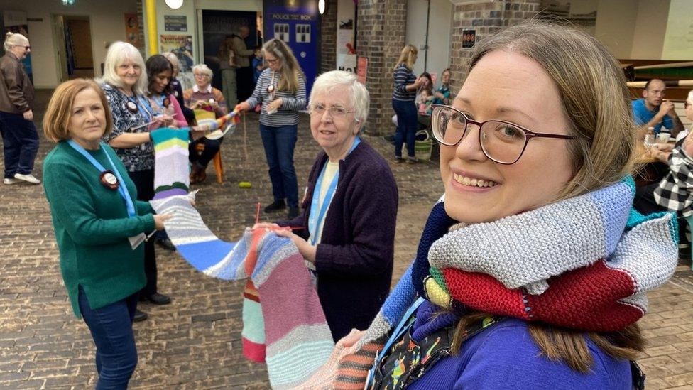 A photo of a group of women holding up the very long scarf and smiling at the camera