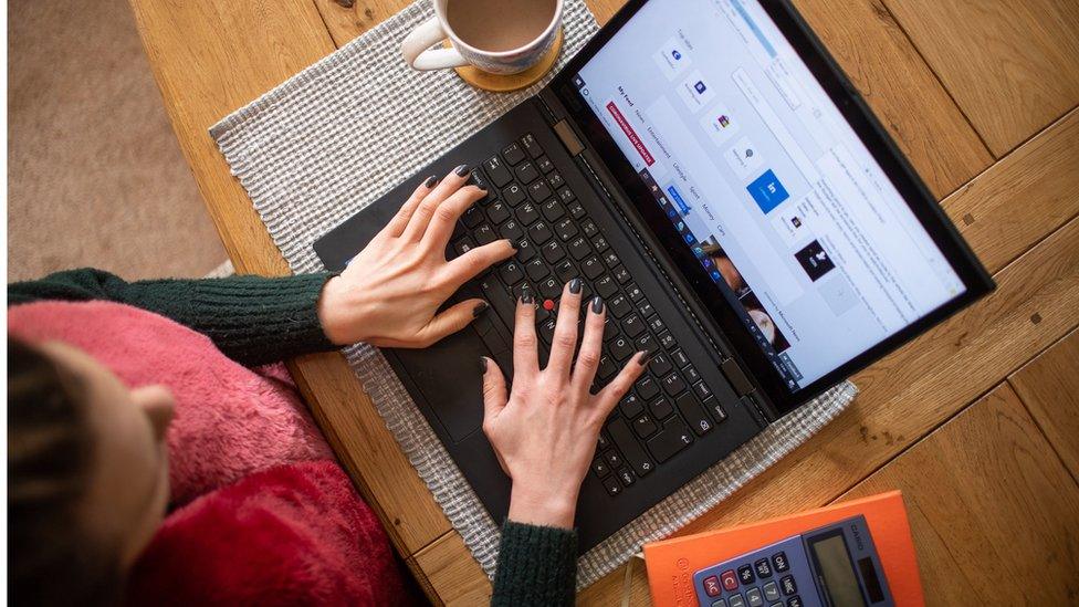 A woman using a laptop on a dining room table set up as a remote office to work from home