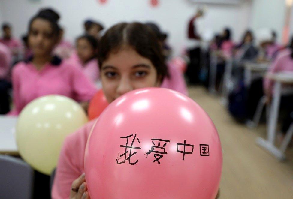 A girl holds a pink balloon that has Chinese script written on it in black marker pen.