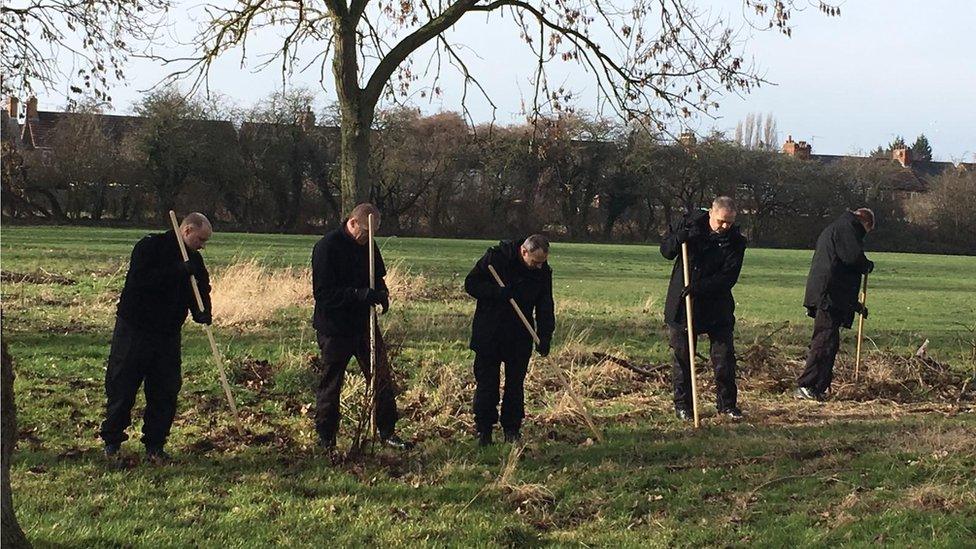 Five men raking leaves on a field