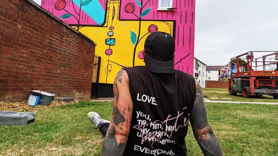 Artist looking up at street art on the side of a house