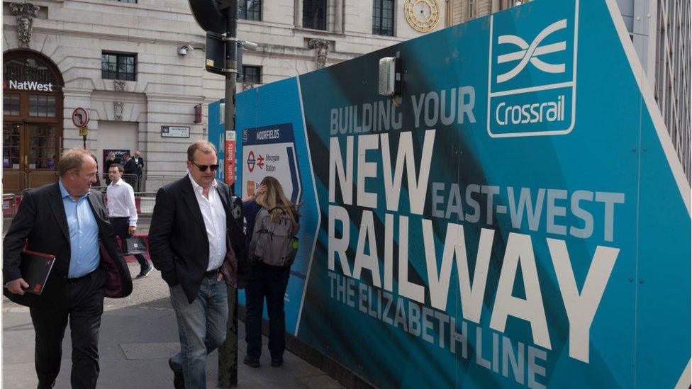 People walk past billboards promoting Crossrail's new Queen Elizabeth rail line in Moorgate, London