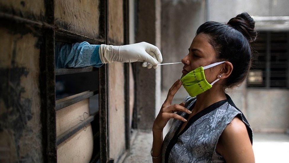 A health official collects a swab sample from a woman to test for the COVID-19