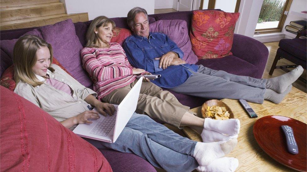 Grandparents watch television while granddaughter uses her laptop