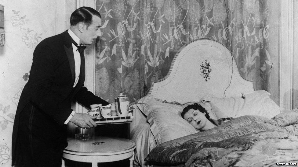 Black and white photo of a butler bringing drinks to a sleeping woman