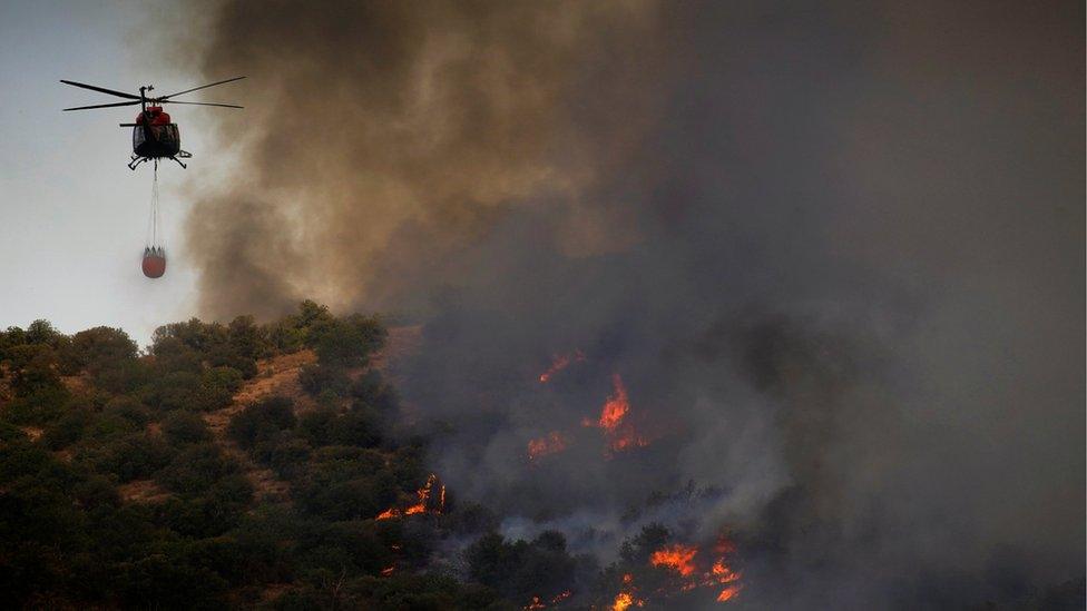 A helicopter flies over a wildfire near the city of Toledo