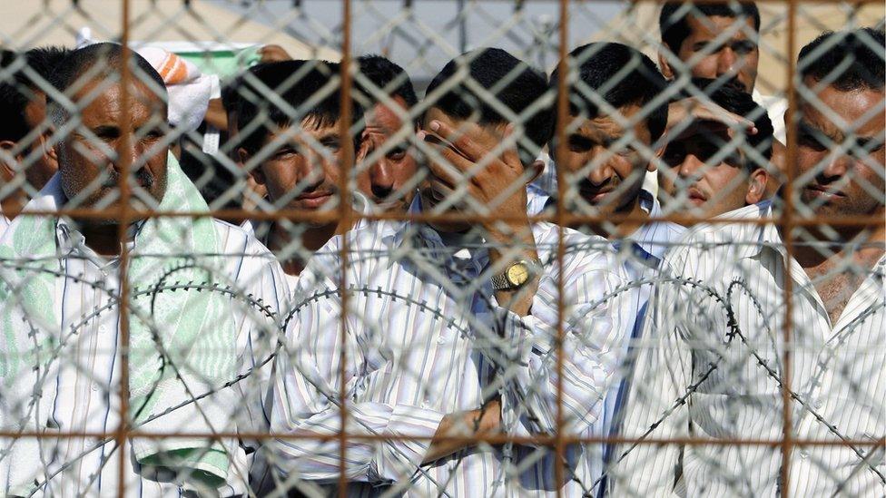 Prisoners at the Abu Ghraib prison near Baghdad watch through a security fence