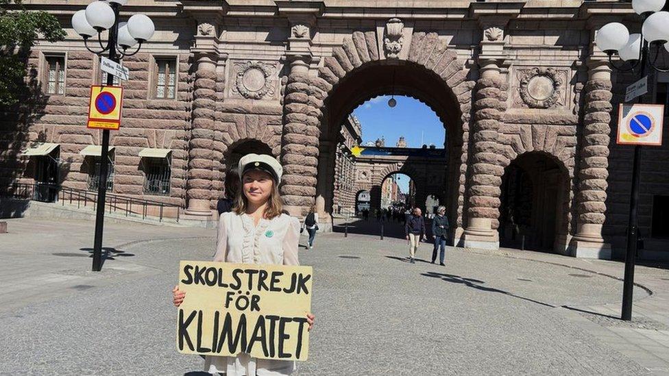 Greta standing outside parliament holding placard