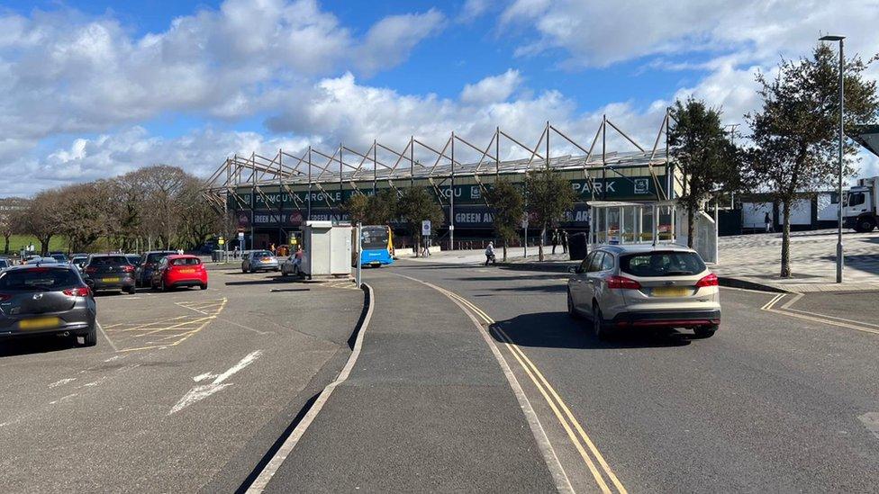 Road running up to stadium and cars moving and parked in spaces