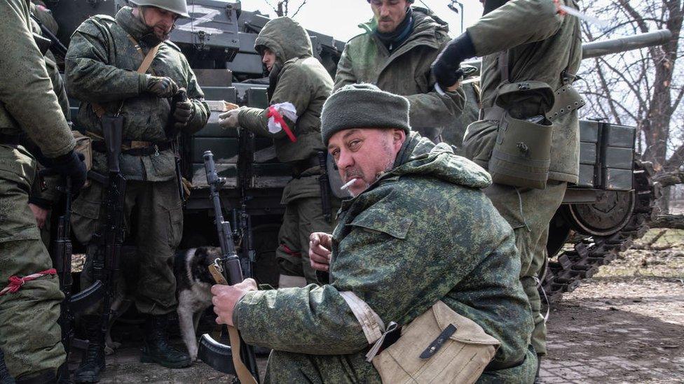 DNR (Donetsk People's Republic) fighters take cover behind an abandoned tank on a frontline position in the centre of Mariupol, 27 March