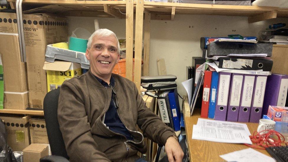 Man sat in his office with filing folders and storage boxes in the background