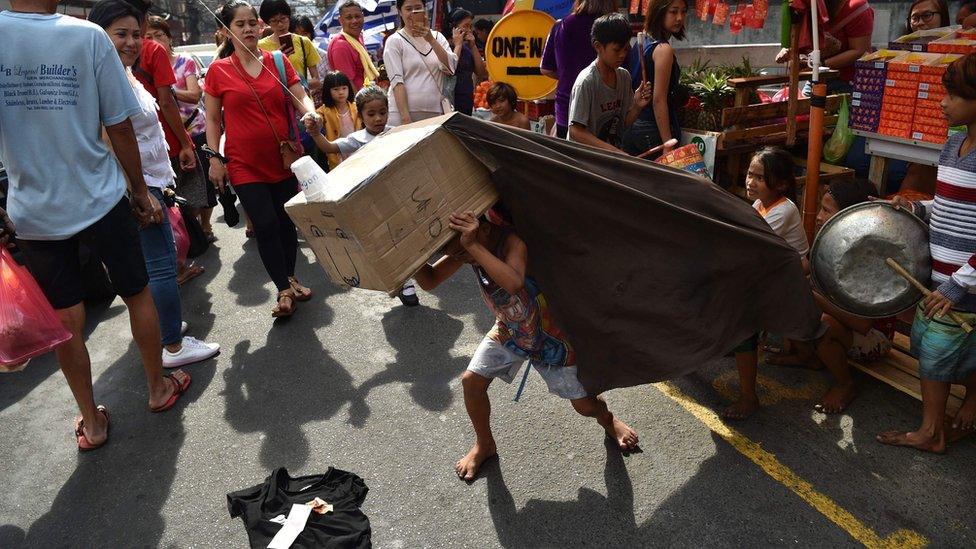 Children perform a lion dance routine with an improvised lion head made from cardboard for pedestrians in the Chinatown district of Manila