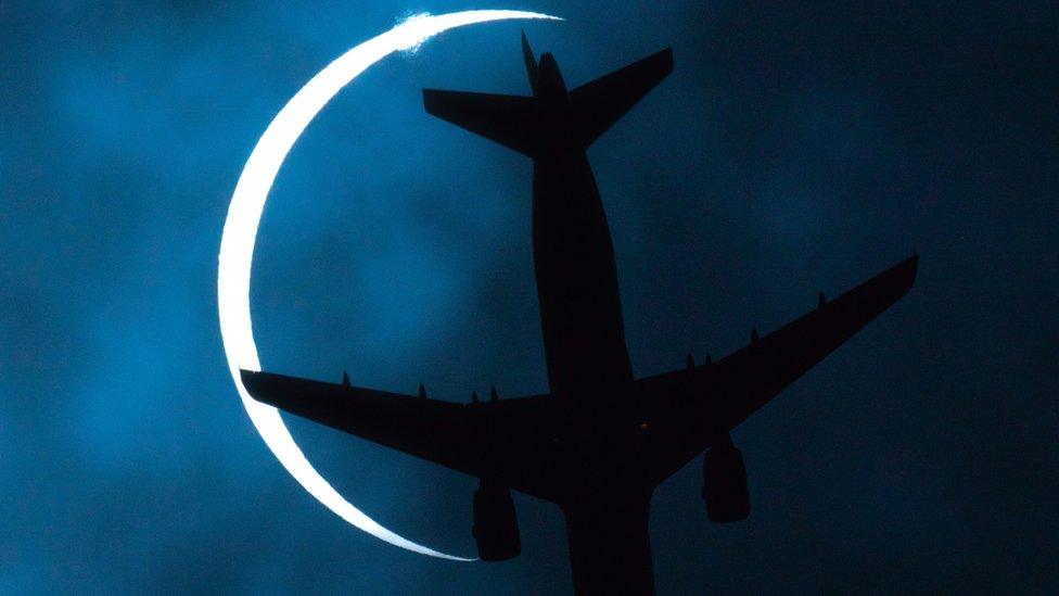 plane-flying-across-the-sky-as-moon-moves-across-sun