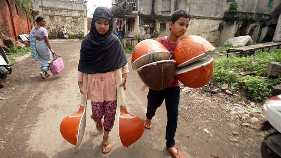 Two children walk down the street carrying sitars