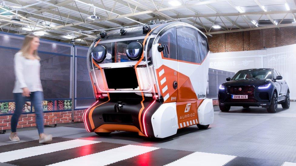 A woman walks across a zebra crossing while looking at a self-driving pod