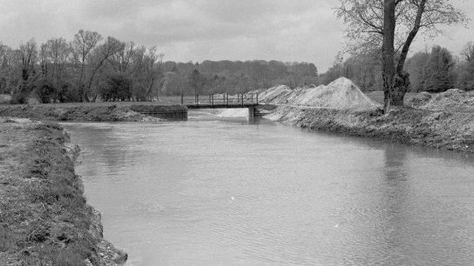 An archive black and white photo of when the River Avon was straightened and dredged, showing piles of debris by the side