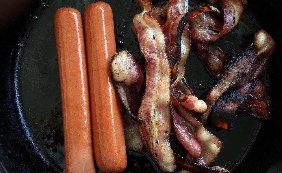 Sausages and bacon frying in a pan