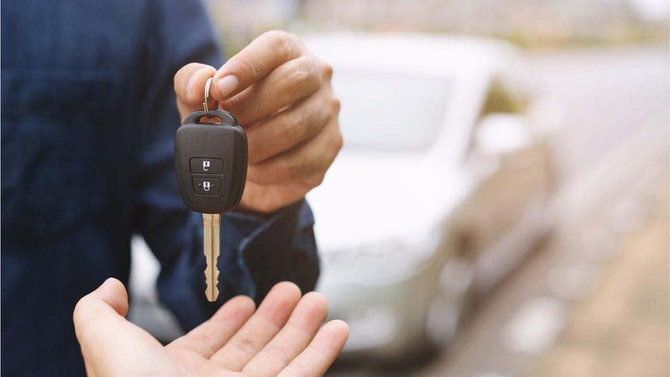 A man handing car keys to a new car owner