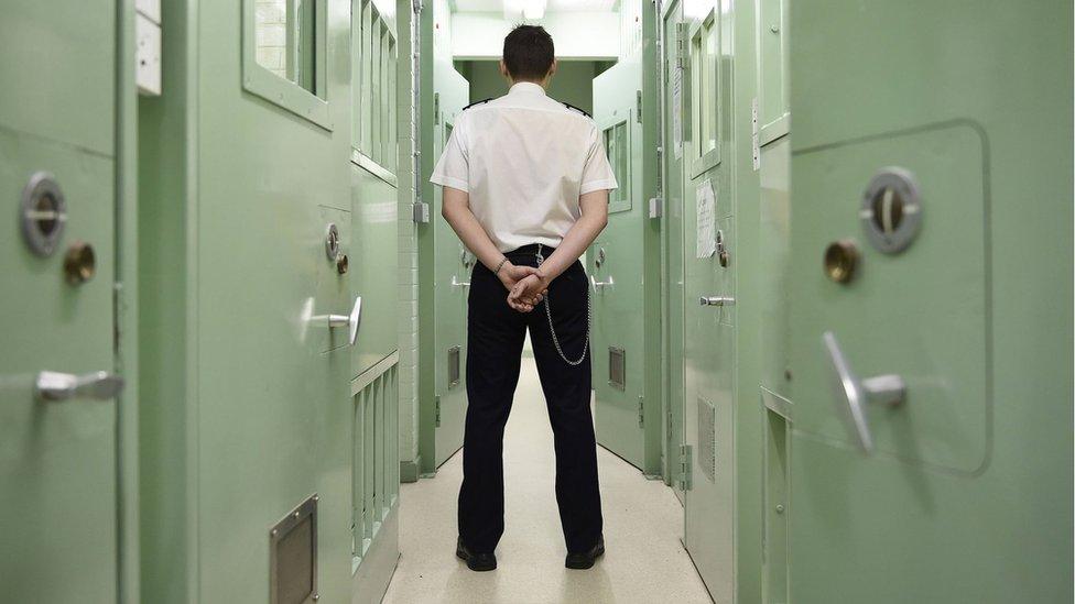 A prison guard stands in the corridor of a prison with his back to the camera.