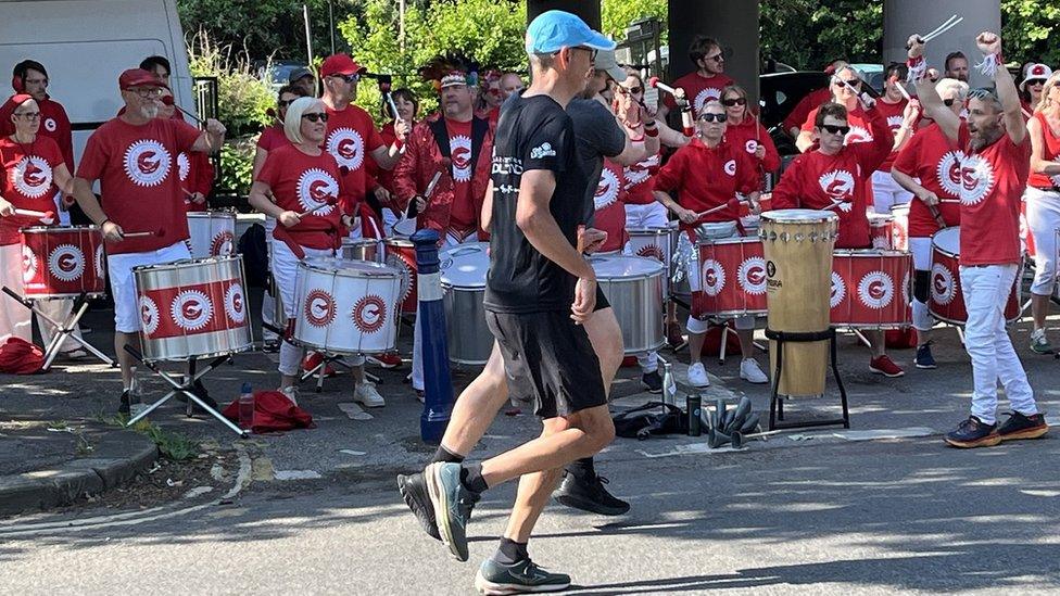 Runners in the Bristol 10k 2024 go past a samba band whose members are dressed in red