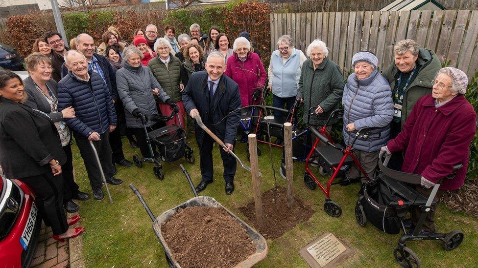 Man planting tree surrounded by crowd