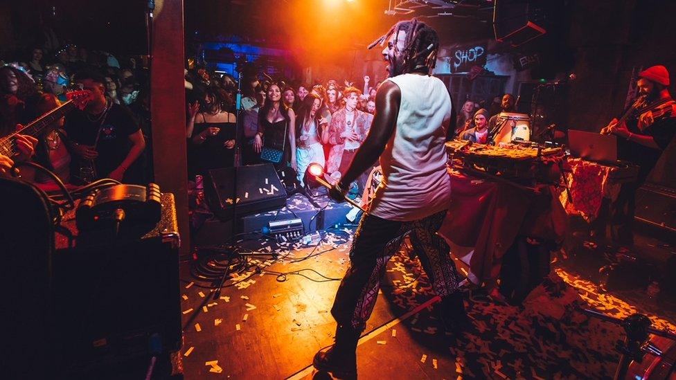 A band performs on stage while the audience watches in the background at Wake the Tiger in Bristol