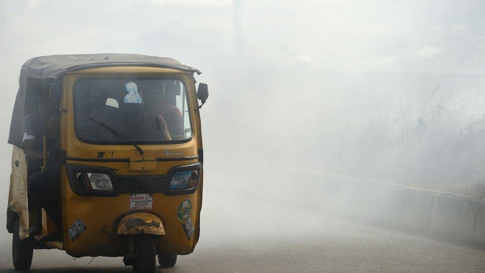 A rickshaw carries passengers through smoke emitted from a dump in the city of Port Harcourt