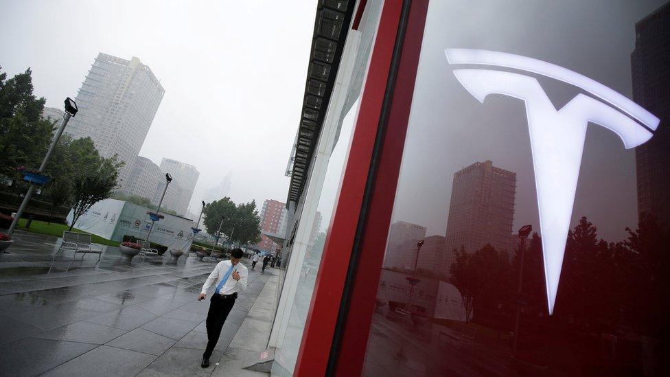 A man walks near a logo of Tesla outside its China headquarters in Beijing