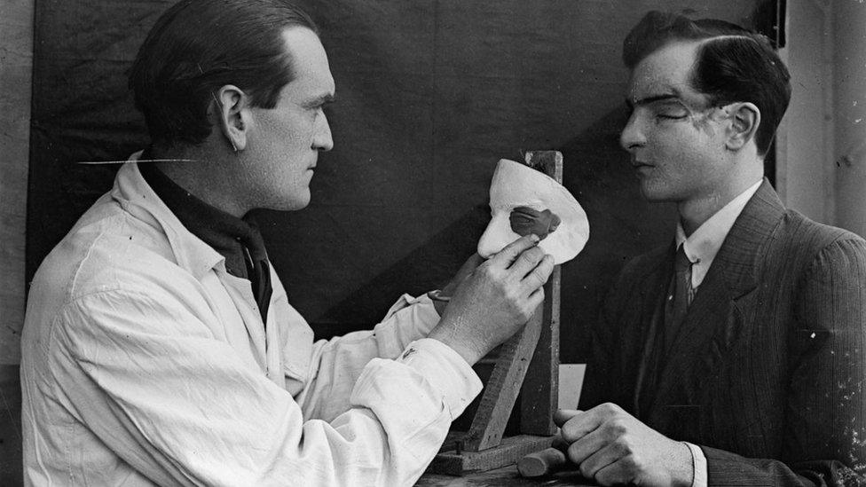 Captain Francis Derwent Wood RA of the Royal Army Medical Corps holds an artist’s palette as he adds the finishing touches to a patient’s new facial plate