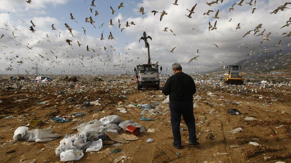 A man stands in front of vehicles arranging piles of garbage at Liosia landfill northeast of Athens