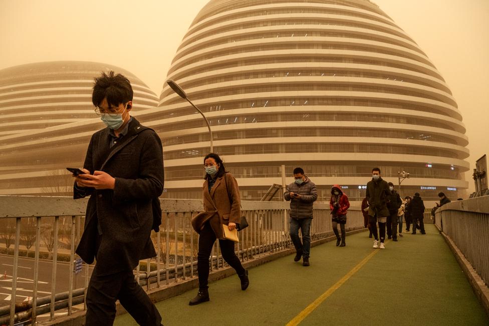 People wear protective masks as they walk during a sandstorm on 15 March 2021 in Beijing