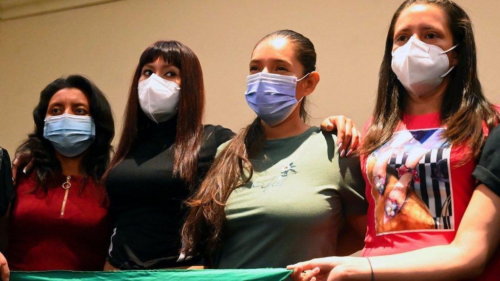 Four Salvadoran women stand together holding a large green handkerchief